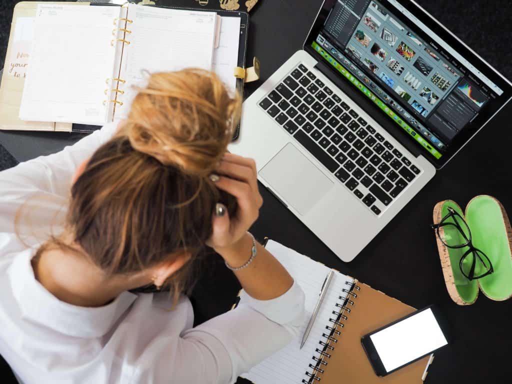 frustrated woman at desk with hand on her head in front of laptop and notebook