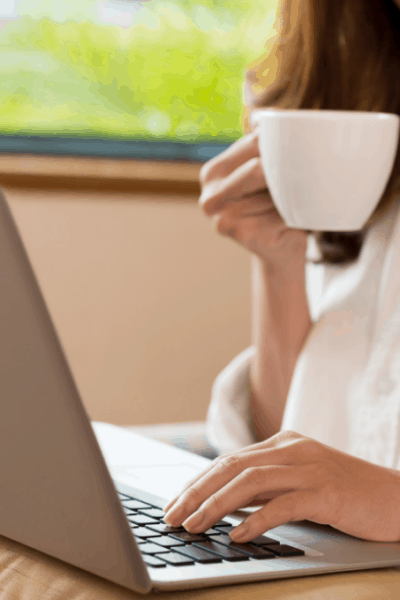 woman drinking coffee working on laptop on cushion on lap
