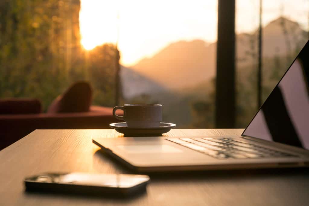 laptop, coffee mug and phone on desk with woman on sofa in background