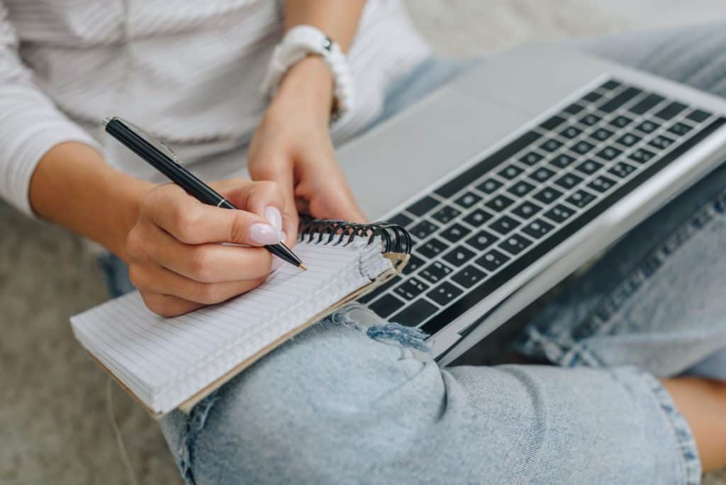 woman sitting on floor with laptop, writing in a notebook