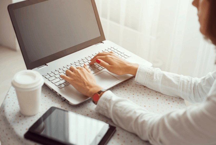 woman at round table working at laptop with coffee, tablet, phone