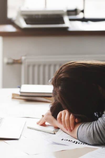 dejected woman with head on desk in front of laptop