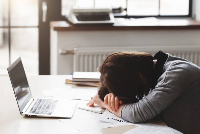 dejected woman with head on desk in front of laptop